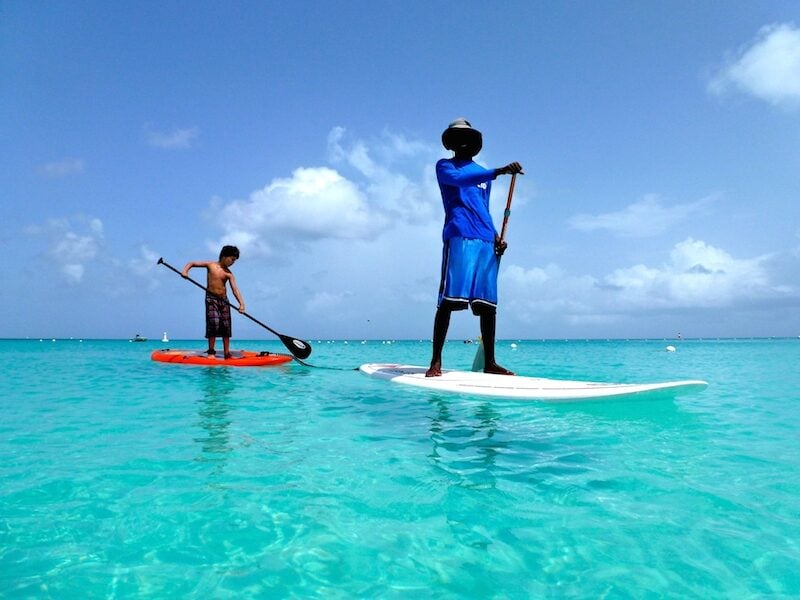 Young boy and guide stand-up paddle-boarding on Grace Bay Beach in Turks and Caicos. 