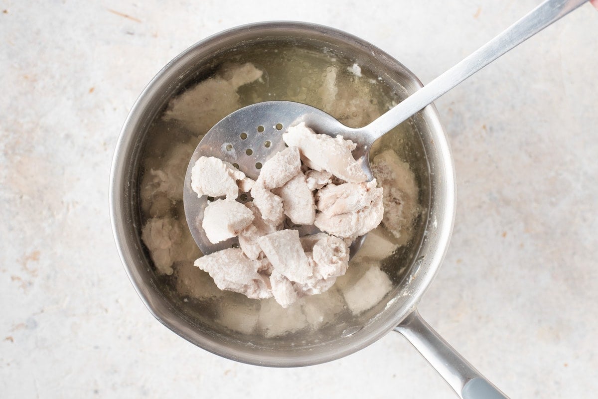 Pieces of chicken cooking in water in a pot.