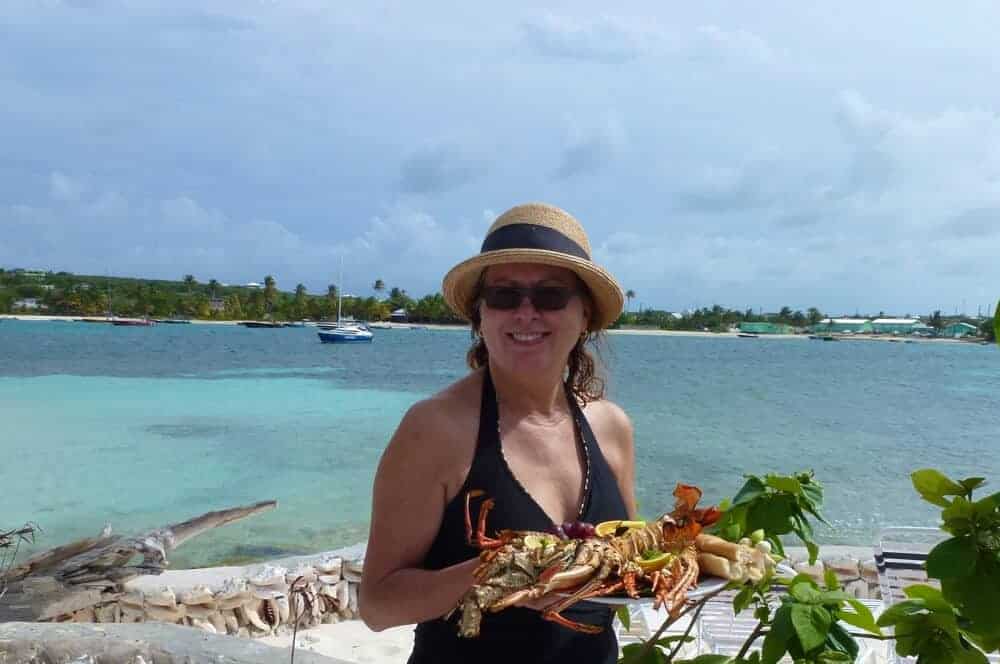 Woman holding a plate of grilled lobster at Scilly Cay, Anguilla. 