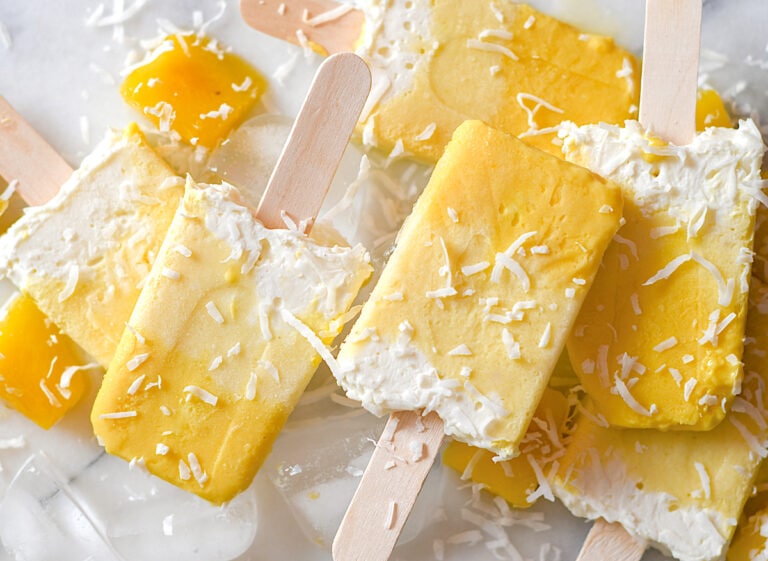 Mango coconut popsicles on a white table.