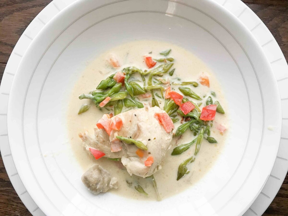 Guatemalan pollo en crema y loroco or Guatemalan chicken in cream of loroco flower) in a white bowl. 