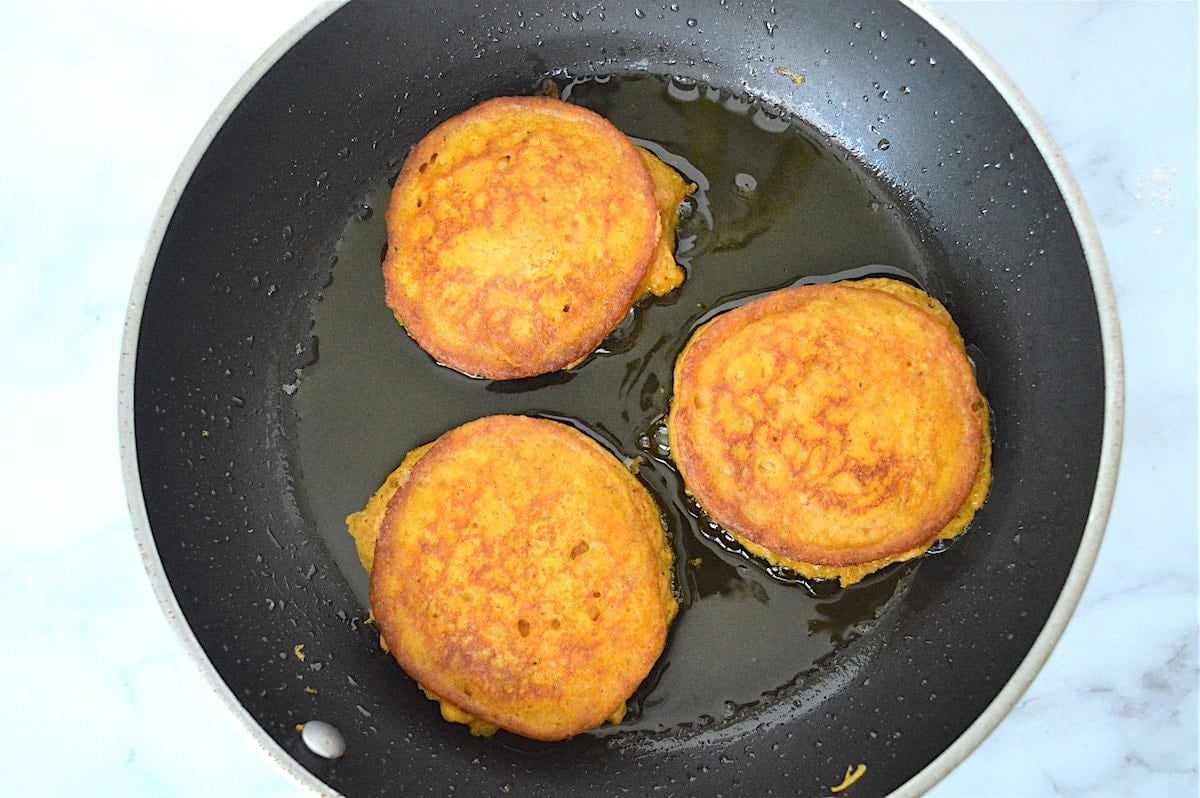 Process shot of flipping Arepa di Papoena pancakes over in a skillet. 