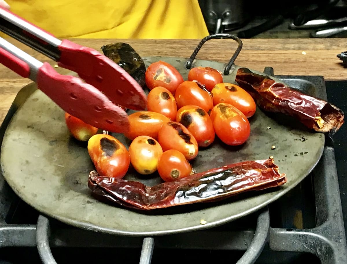 Charring tomatoes and guaque chile on a comal in Guatemala. To