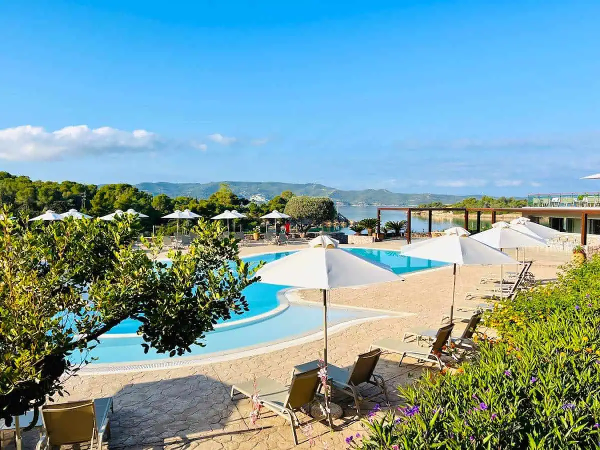 Beach chairs around pool with umbrellas and trees. 