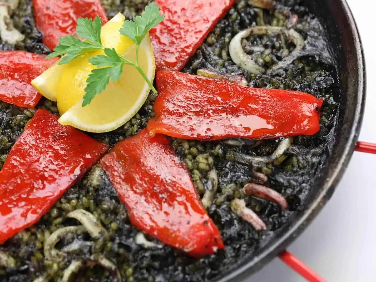 Black paella topped with strips of red pepper. 