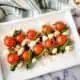 Caprese salad skewers on a platter with balsamic vinegar over the top.