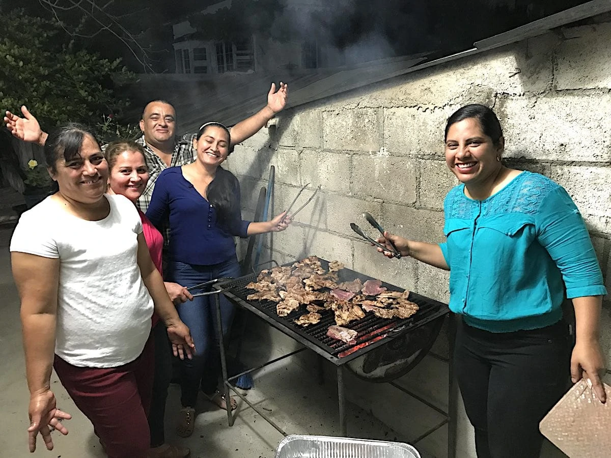 People grilling meat over charcoal at a party is a good example of Guatemalan food culture. 
