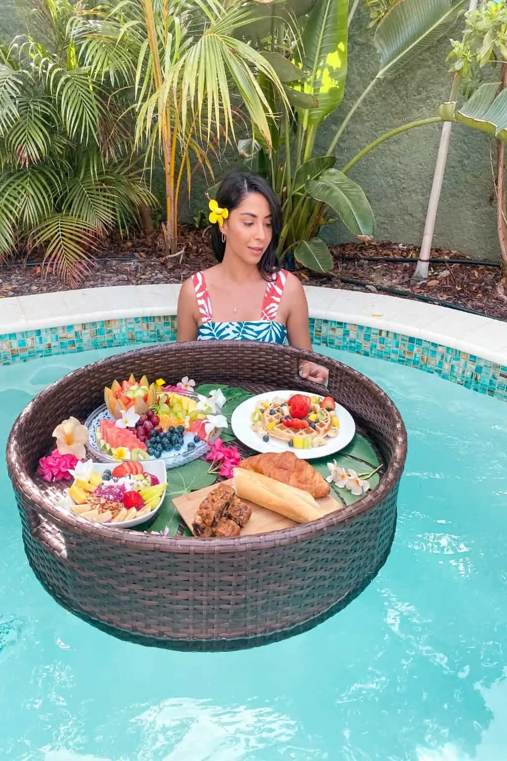 Brunch food on plates floating on a large tray in an outdoor pool with a woman next to it