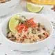 Caribbean rice and red beans in a white bowl garnished with thyme, red pepper and lime wedge.