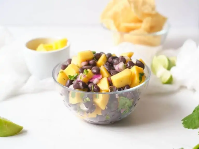 Clear bowl of mango black bean salsa on a white table.