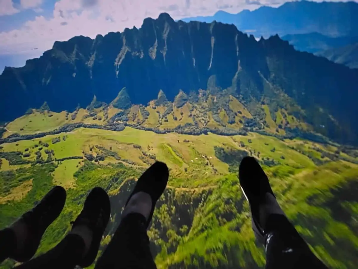 Zip lining over green fields in Hawaii with blue mountains in the background.