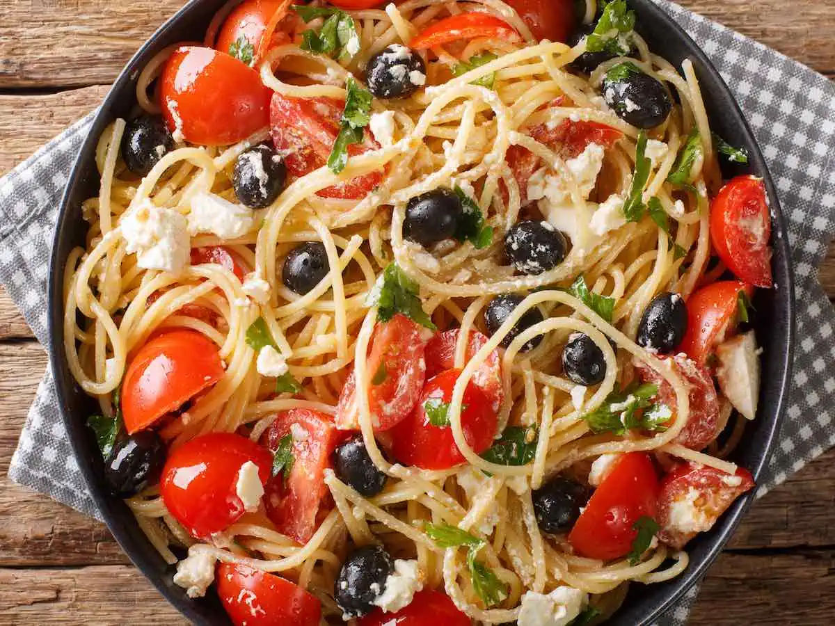 Black bowl of Greek pasta with kalamata olives, tomatoes and spaghetti.   