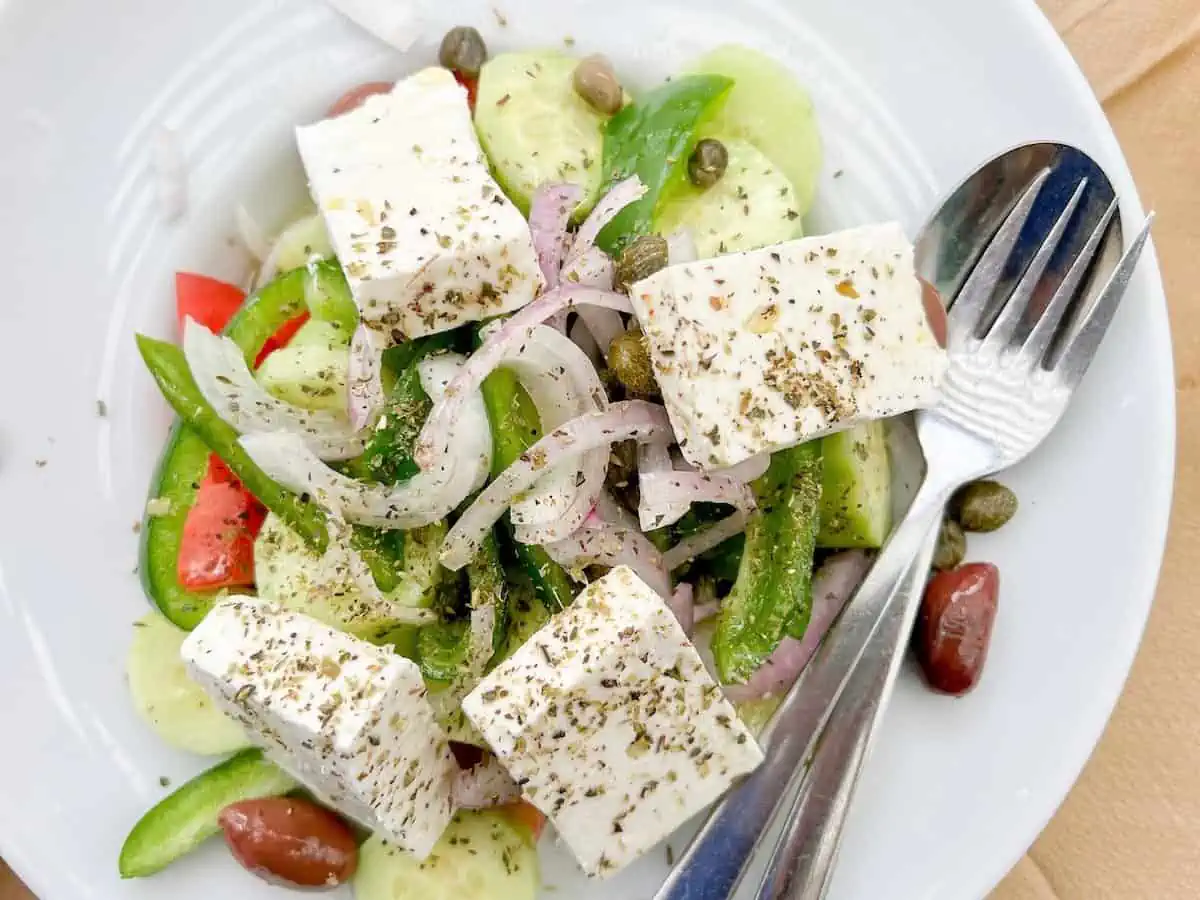 Greek salad with capers and Kalamata olives and feta cheese in a white bowl. 