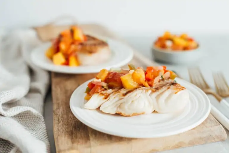 two pieces of grilled halibut with peach salsa on white plates.