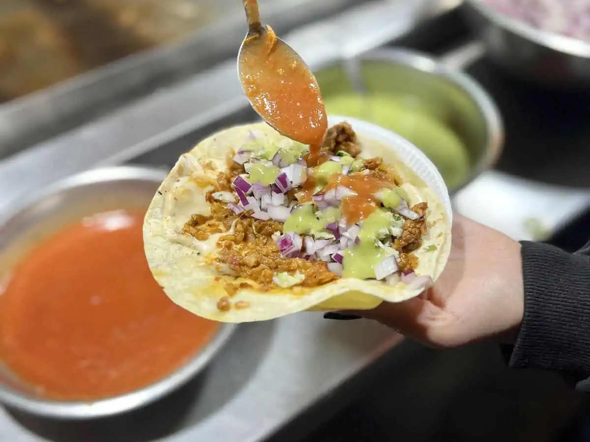 A person adding hot sauce to a gringa, a popular Guatemalan street food. 