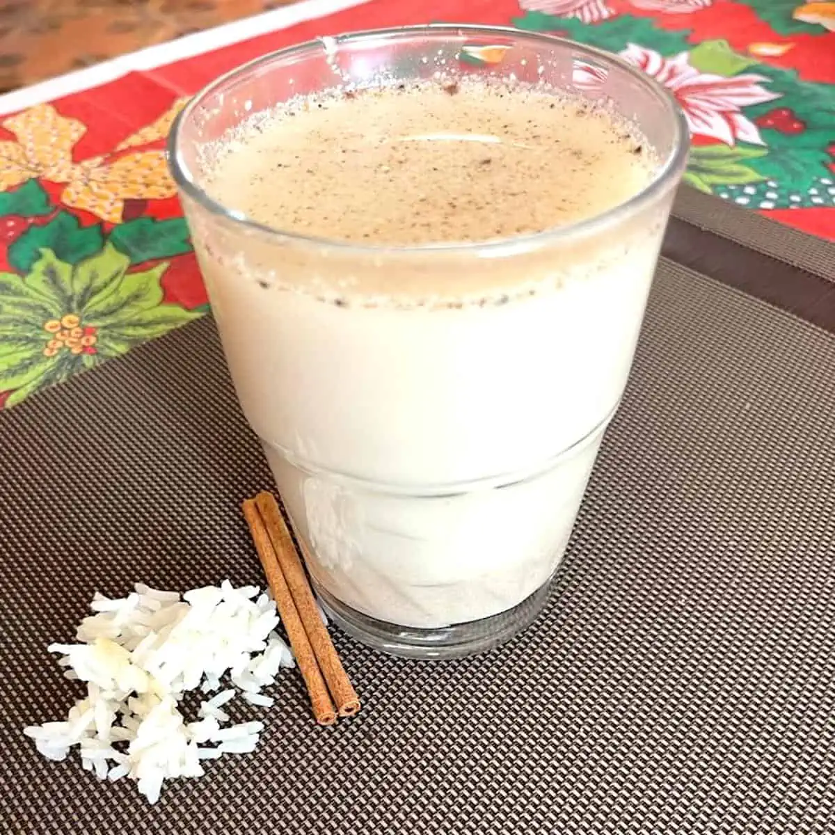 Horchata served with a cinnamon stick on a brown tablecloth.