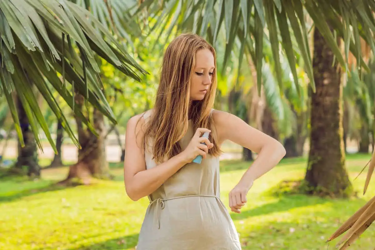 Woman spraying insect repellent on skin outdoor.