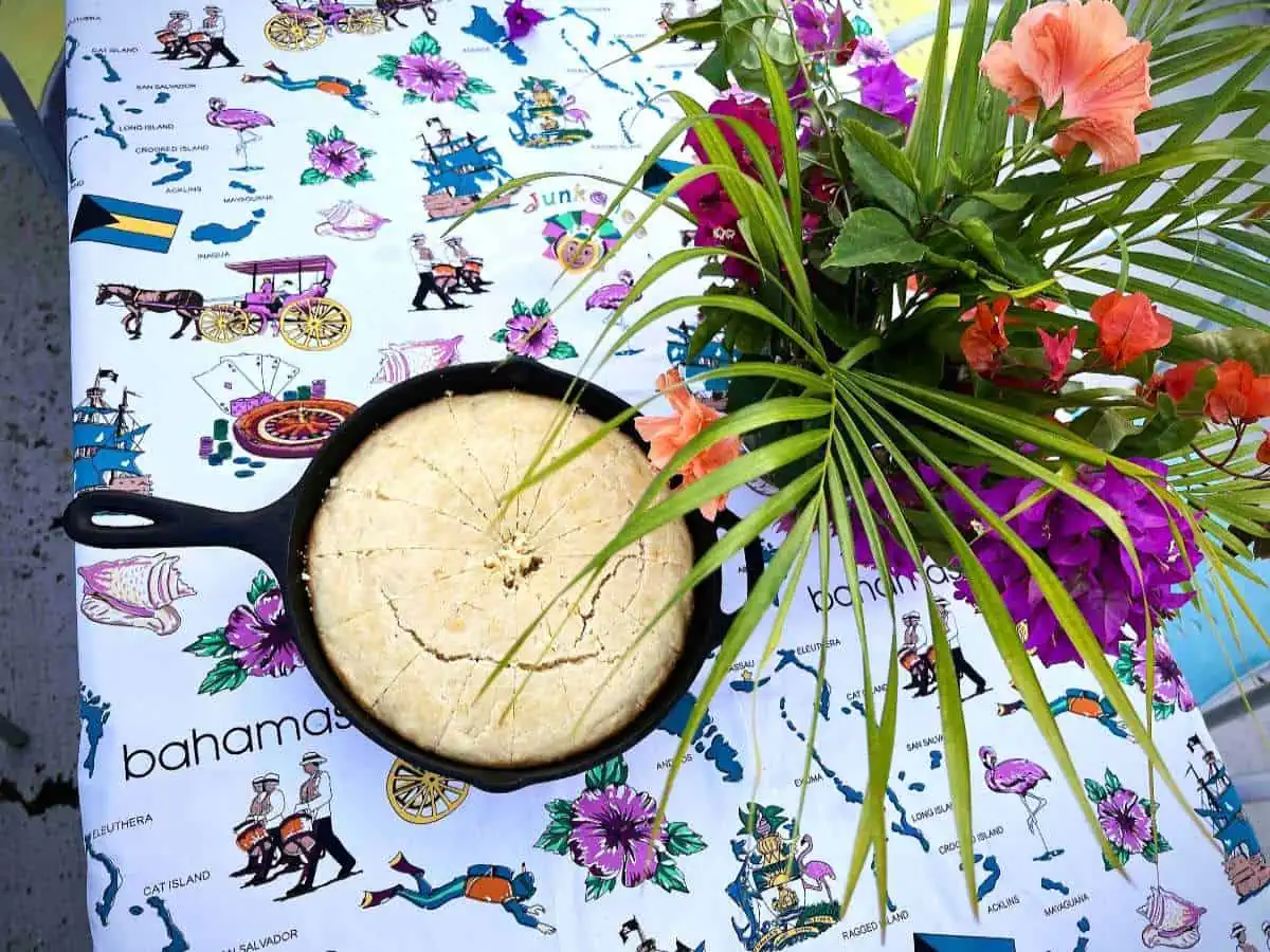 Johnny cake in cast iron skillet on table with plant. 