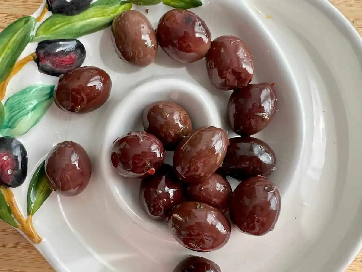 Whole Kalamata olives in a white bowl decorated with black olives. 