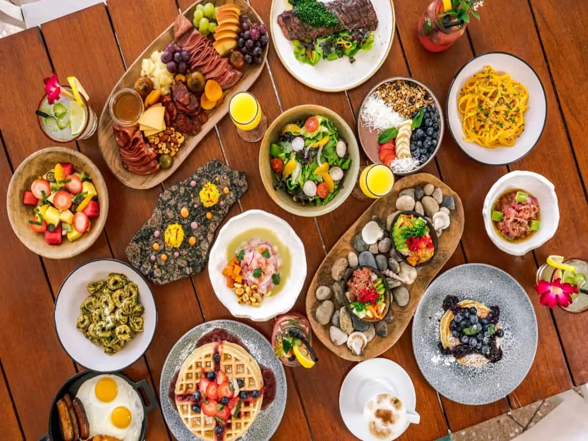 Many plates of brunch foods on a rich wood table