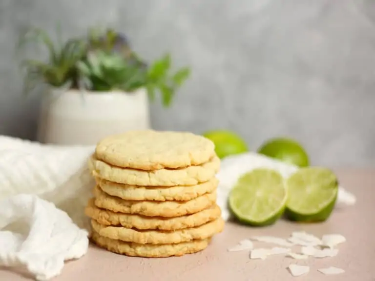 Lime coconut cookies in a stack on a table with fresh limes.