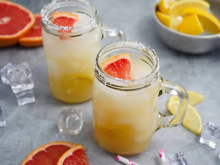 Homemade mezcal paloma cocktails on the table with fresh grapefruit slices and lemon wedges.