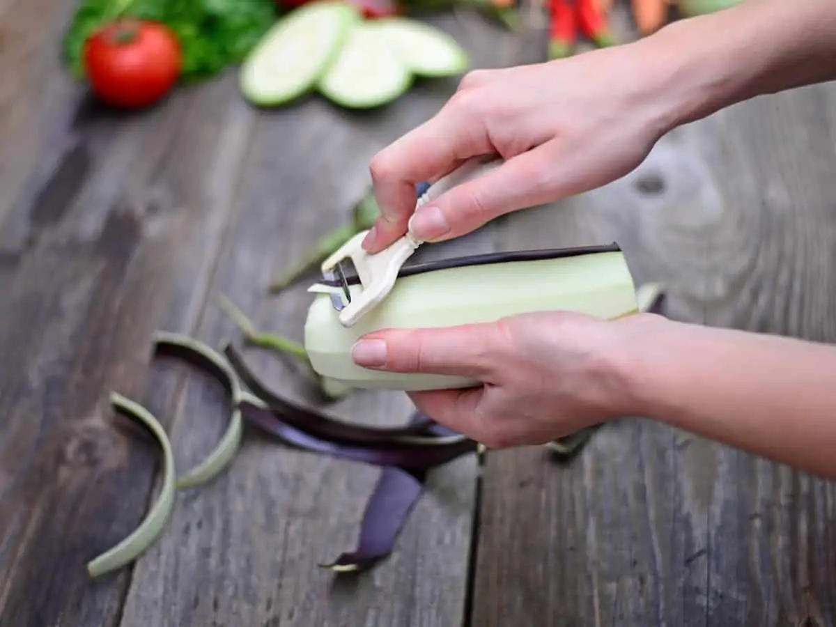 Woman's hand peeling fresh eggplant.