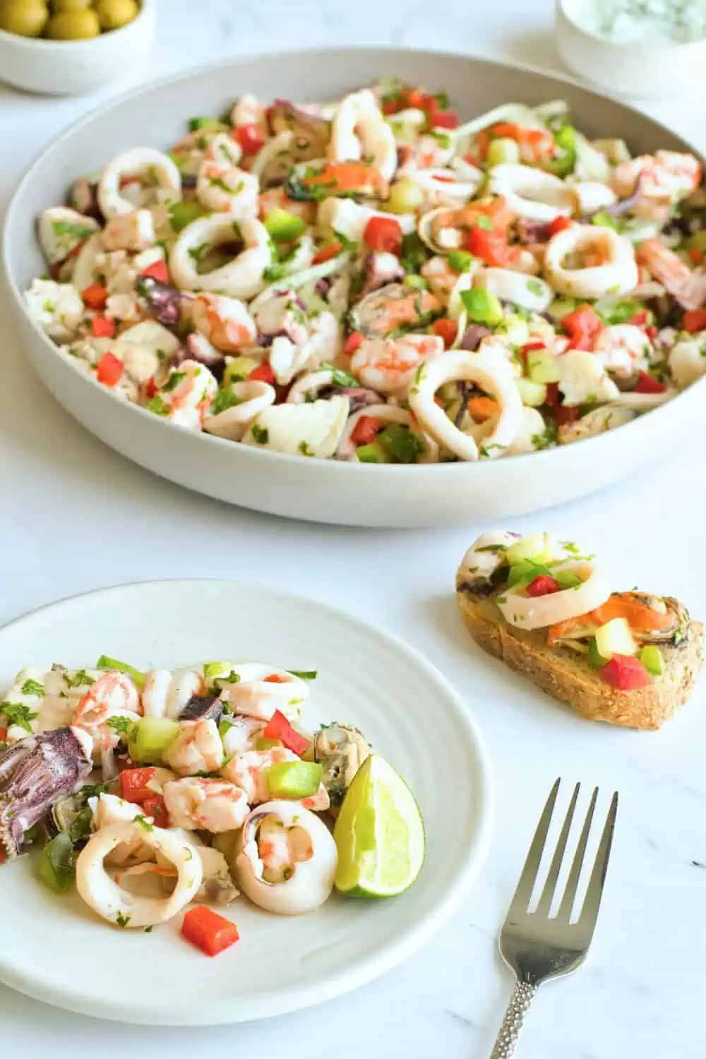 A serving of salpicón de mariscos on a white plate and with a crostini. 