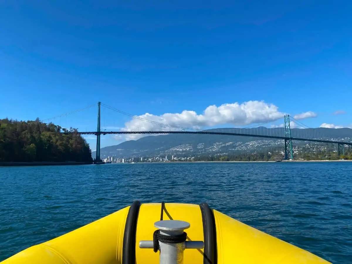 The view of a blue ocean from the bow of a yellow pontoon boat with a bridge in the background.