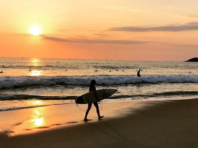 Surfer with board on a beach at sunset in Puerto Escondido, Oaxaca, Mexico.